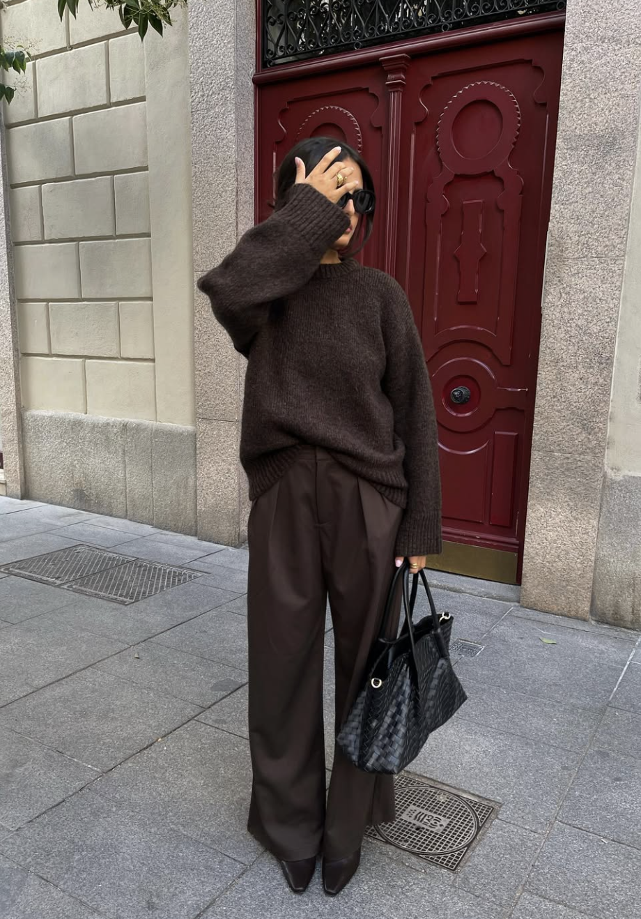 A woman wearing a modern utility outfit featuring a cropped black leather bomber jacket tucked into high-waisted wide-leg trousers, styled with a structured black top-handle bag.