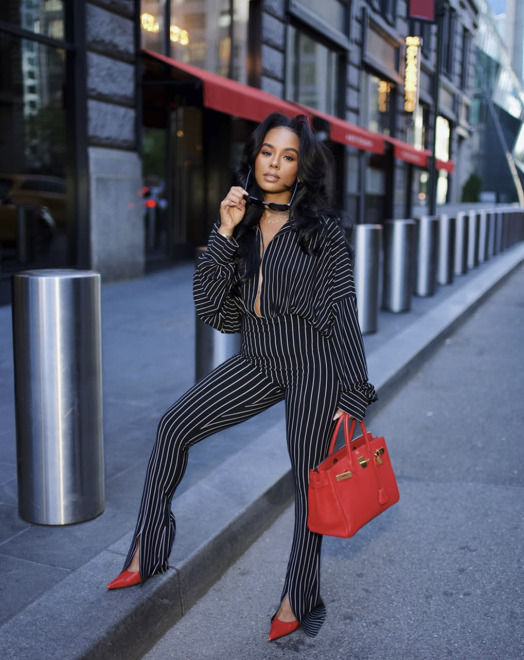 Woman wearing a black and white pinstripe suit with red pointed-toe pumps and holding a red leather handbag on a NYC street during New York Fashion Week.