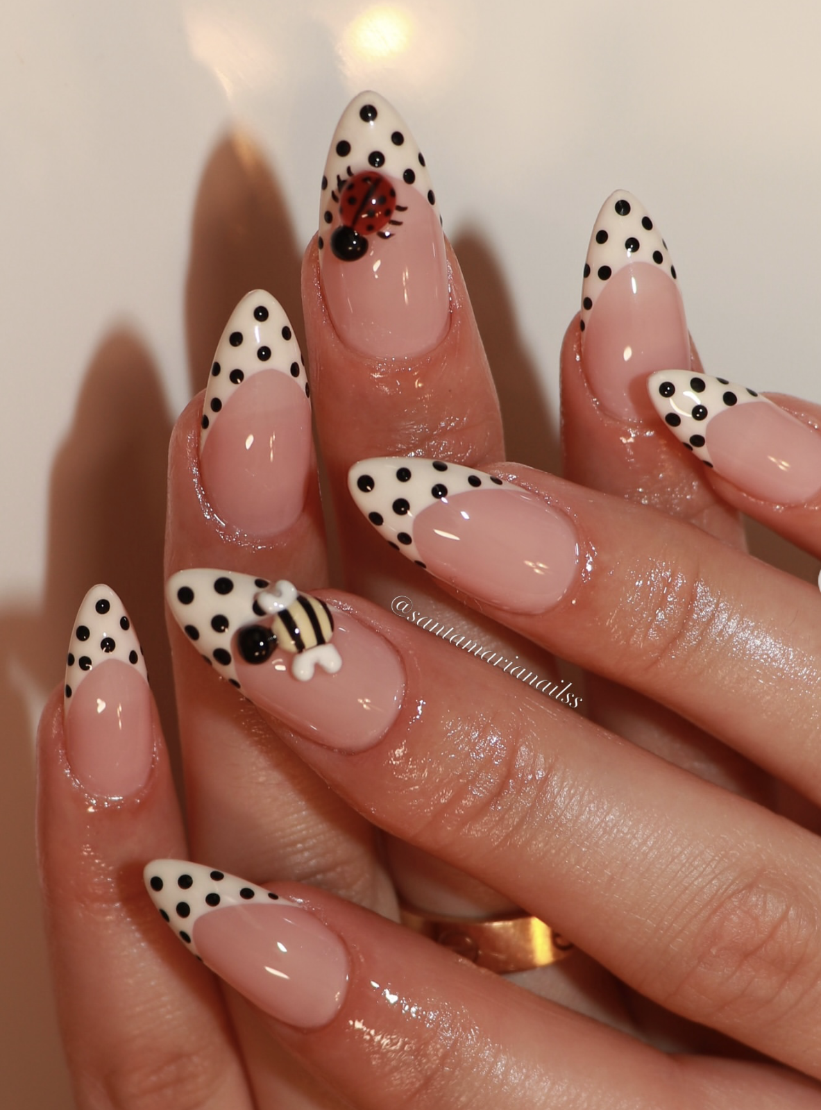 Long almond nails with white French tips, black polka dots, and hand-painted ladybug and bee designs with a 3D charm.