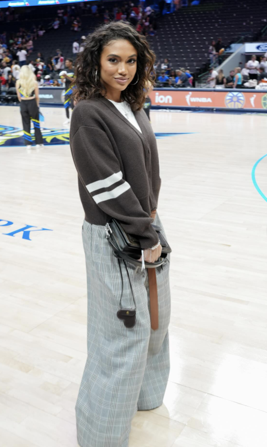 Woman wearing an oversized navy New York sweatshirt with camo cargo pants and a structured handbag.