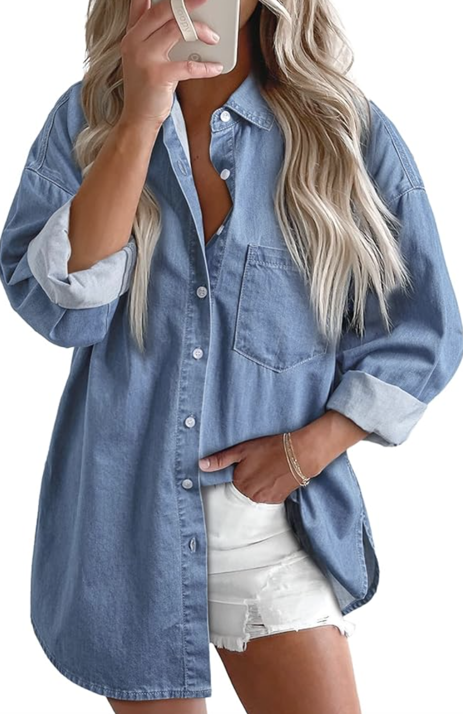 A close-up street style shot of a woman wearing an oversized, light-wash denim button-down shirt with the sleeves rolled up, styled over a casual outfit while holding a smartphone.