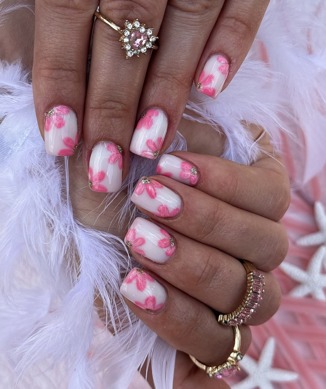 Square white nails with abstract hand-painted pink flowers and gold glitter centers.