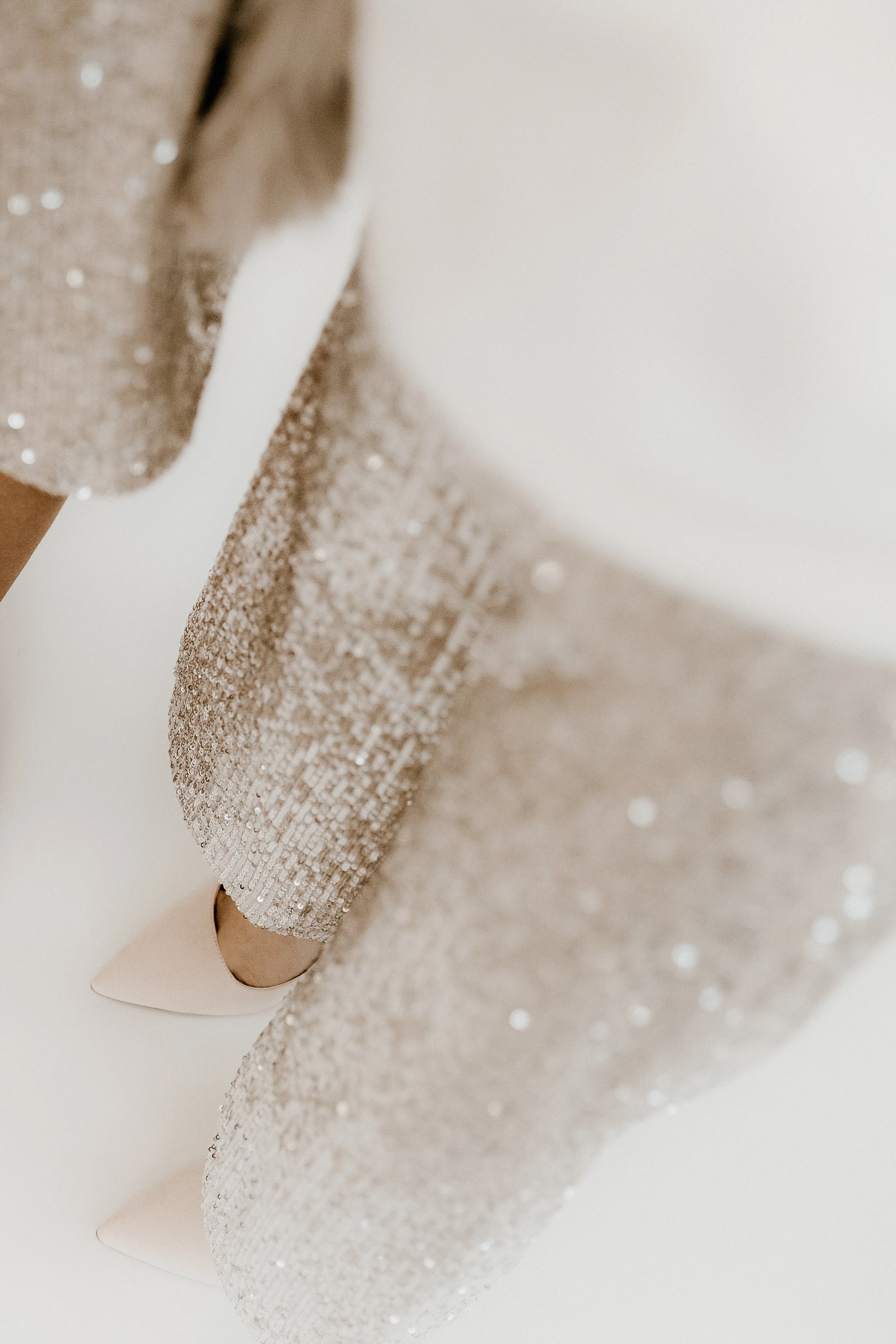 Close-up of someone's legs wearing sparkling, glittering high-heeled shoes and a silver sequined dress.