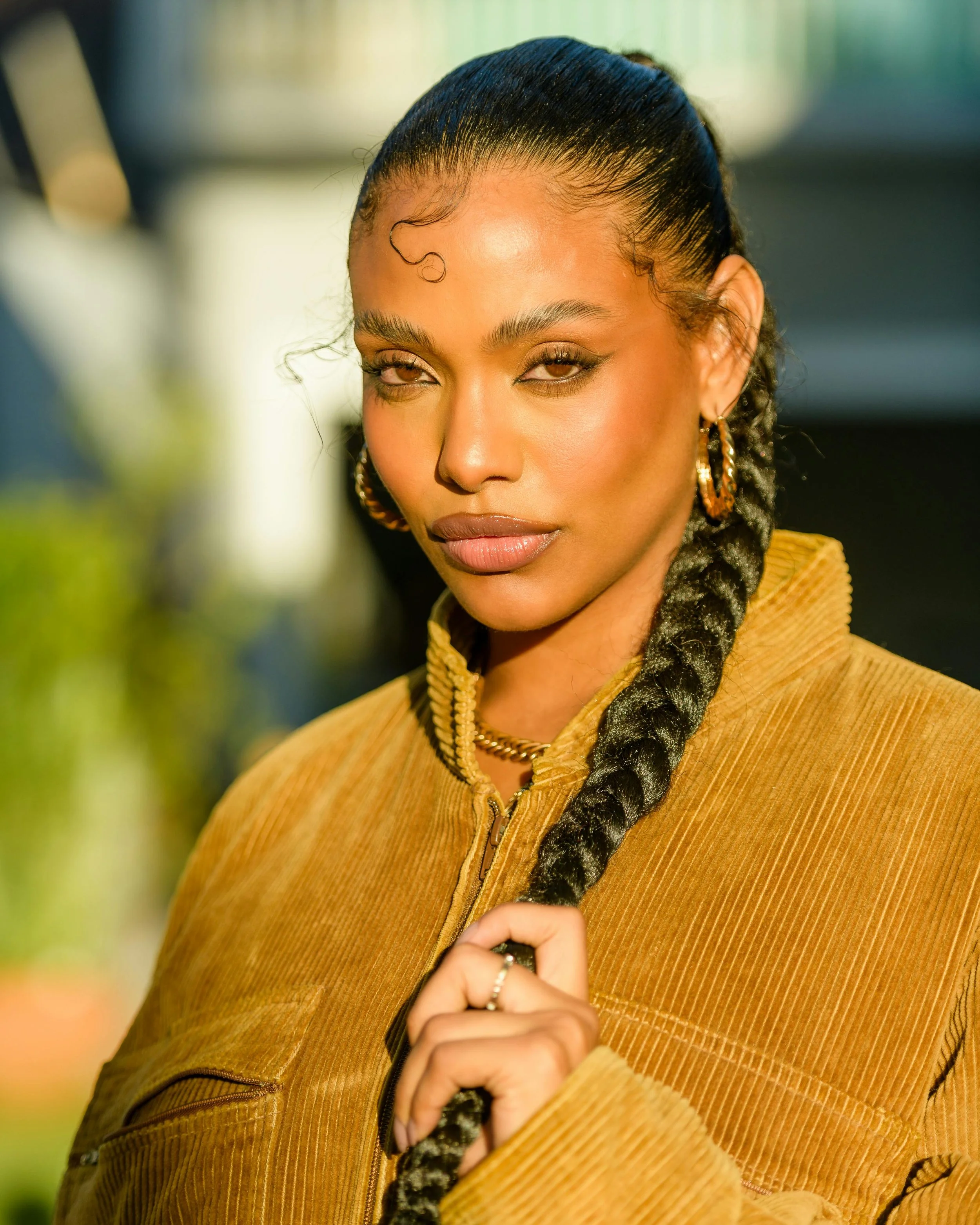 Close up of a woman with sleek, laid edges and a long dark braid wearing a tan corduroy jacket.