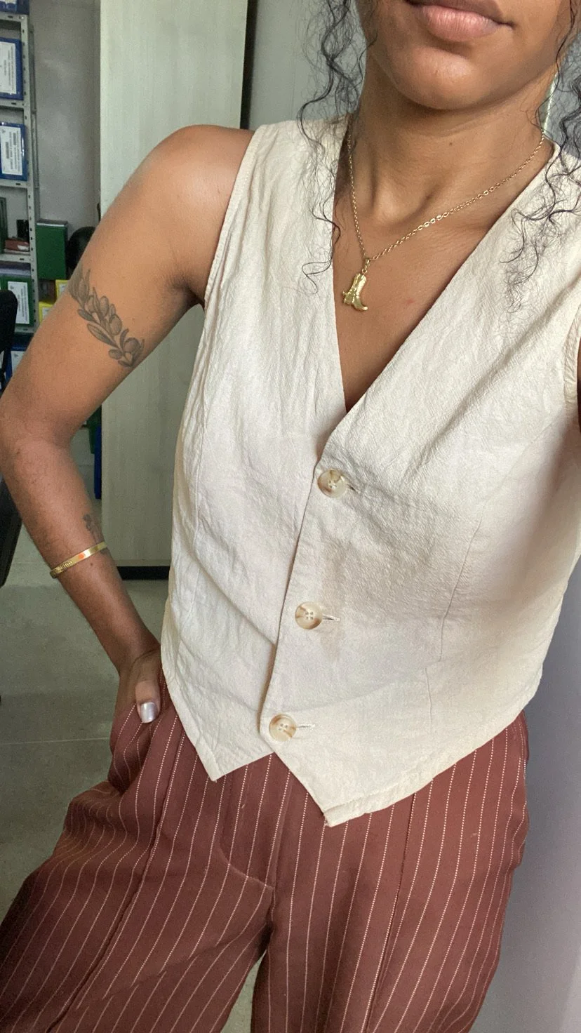 A close-up of a person wearing a cream linen button-up vest paired with reddish-brown pinstriped linen trousers, featuring pearl-style buttons and a tailored fit.