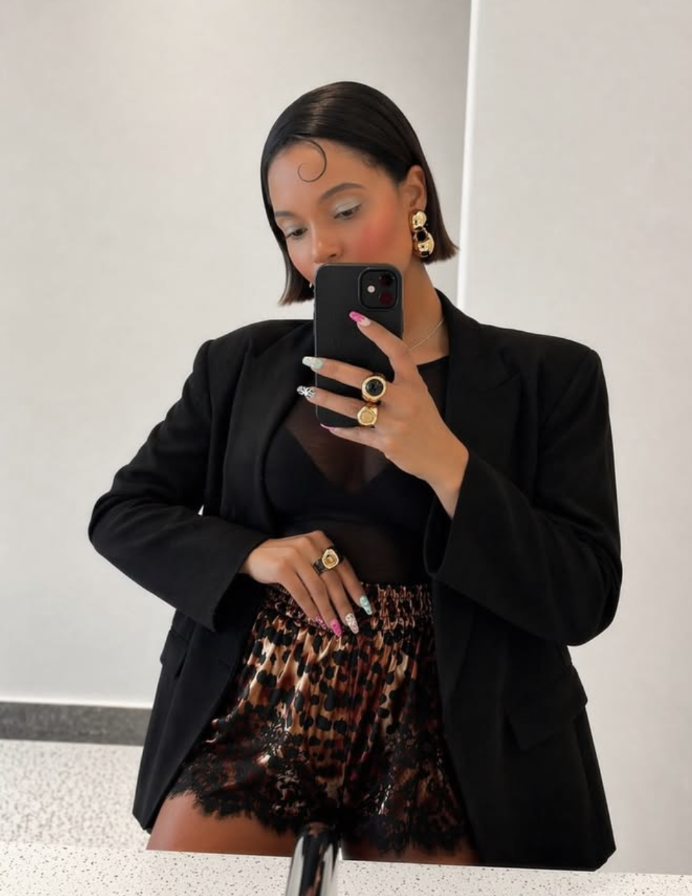 A woman styling leopard print satin shorts with black lace trim, paired with a black oversized blazer for a chic evening look.