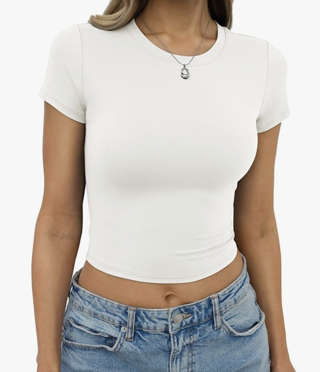 A person wearing a fitted white cropped t-shirt and classic blue denim jeans with a silver pendant necklace.