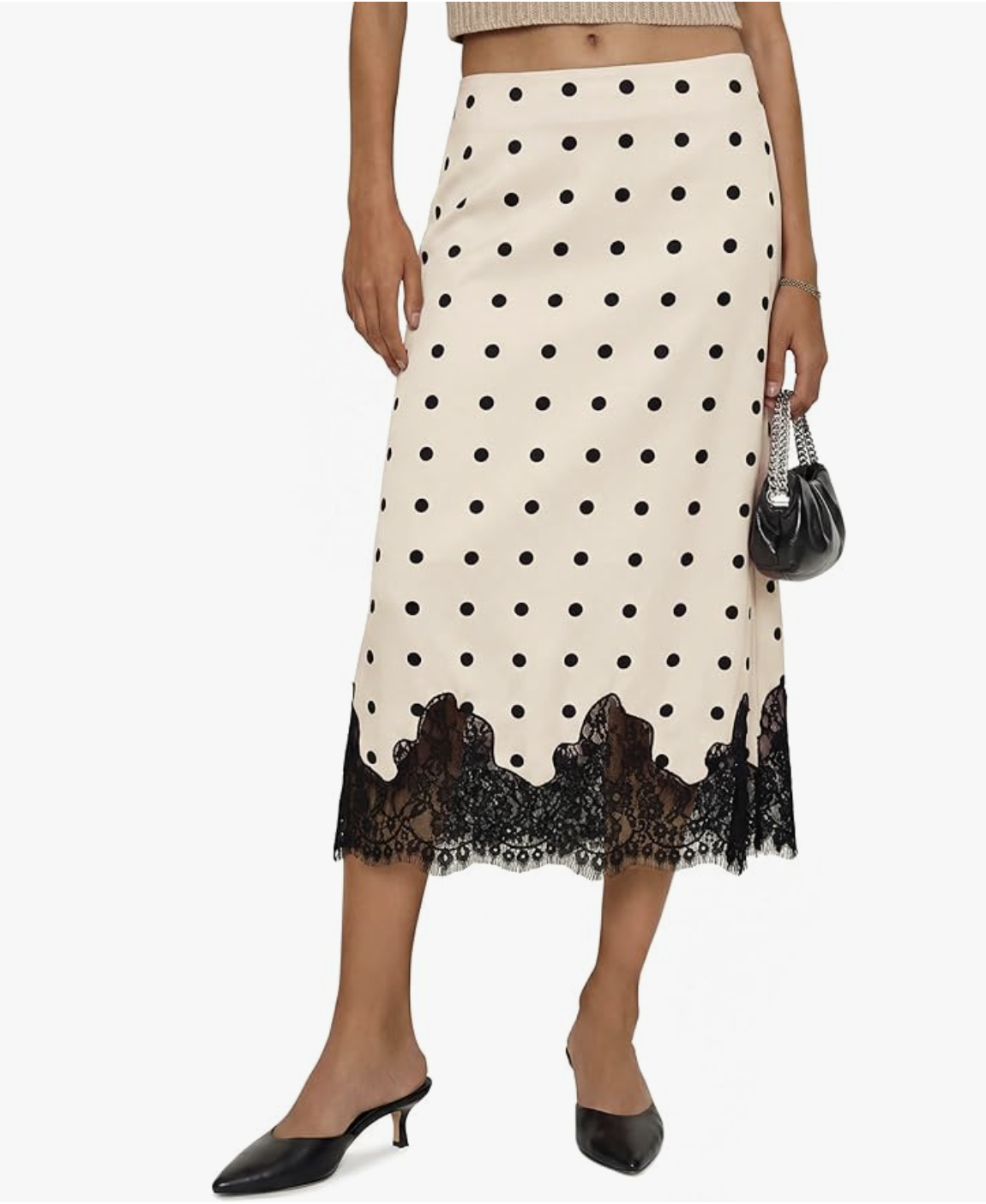 A close-up of a cream-colored satin midi skirt featuring black polka dots and a scalloped black lace trim at the hem, styled with black kitten heels.