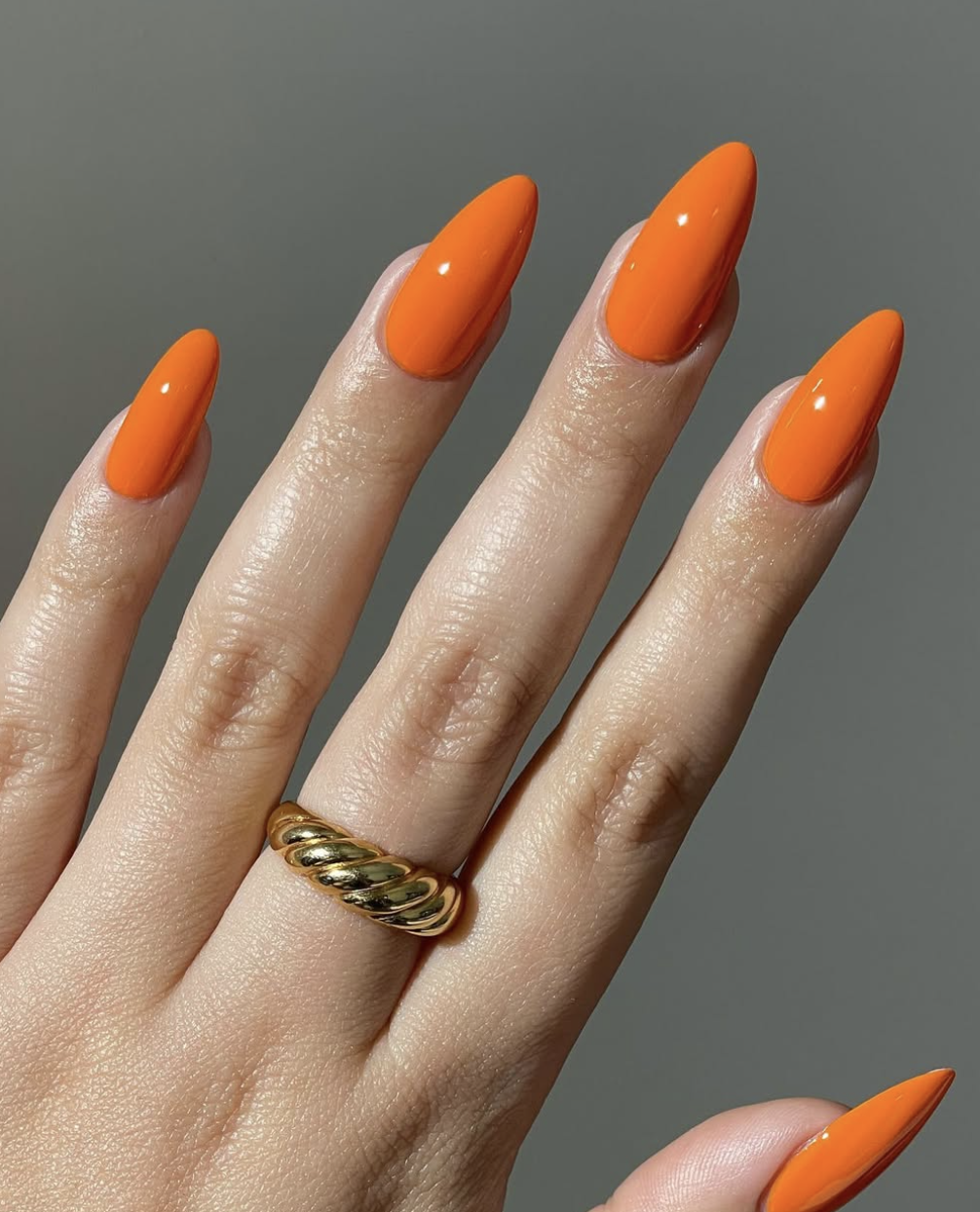 A vibrant, high-gloss orange manicure on long almond-shaped nails, a trending summertime nail color for 2026.