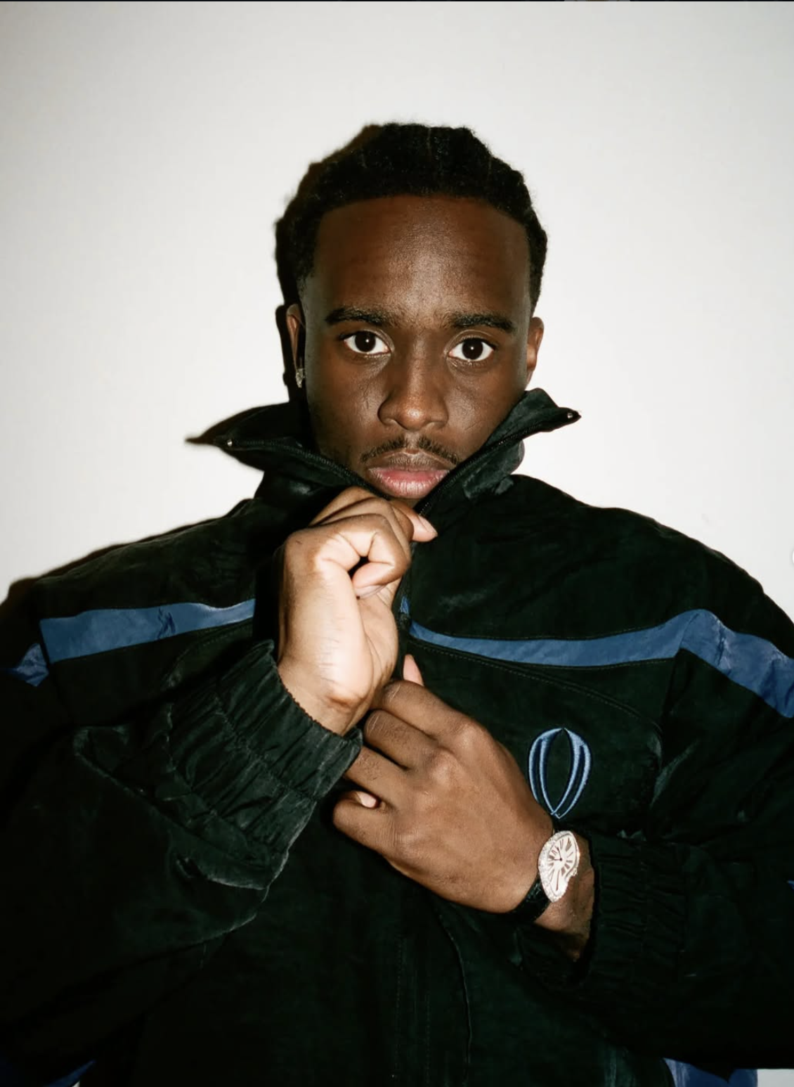 Kai Cenat wearing a black VIVET jacket with blue stripe details and a raised collar.