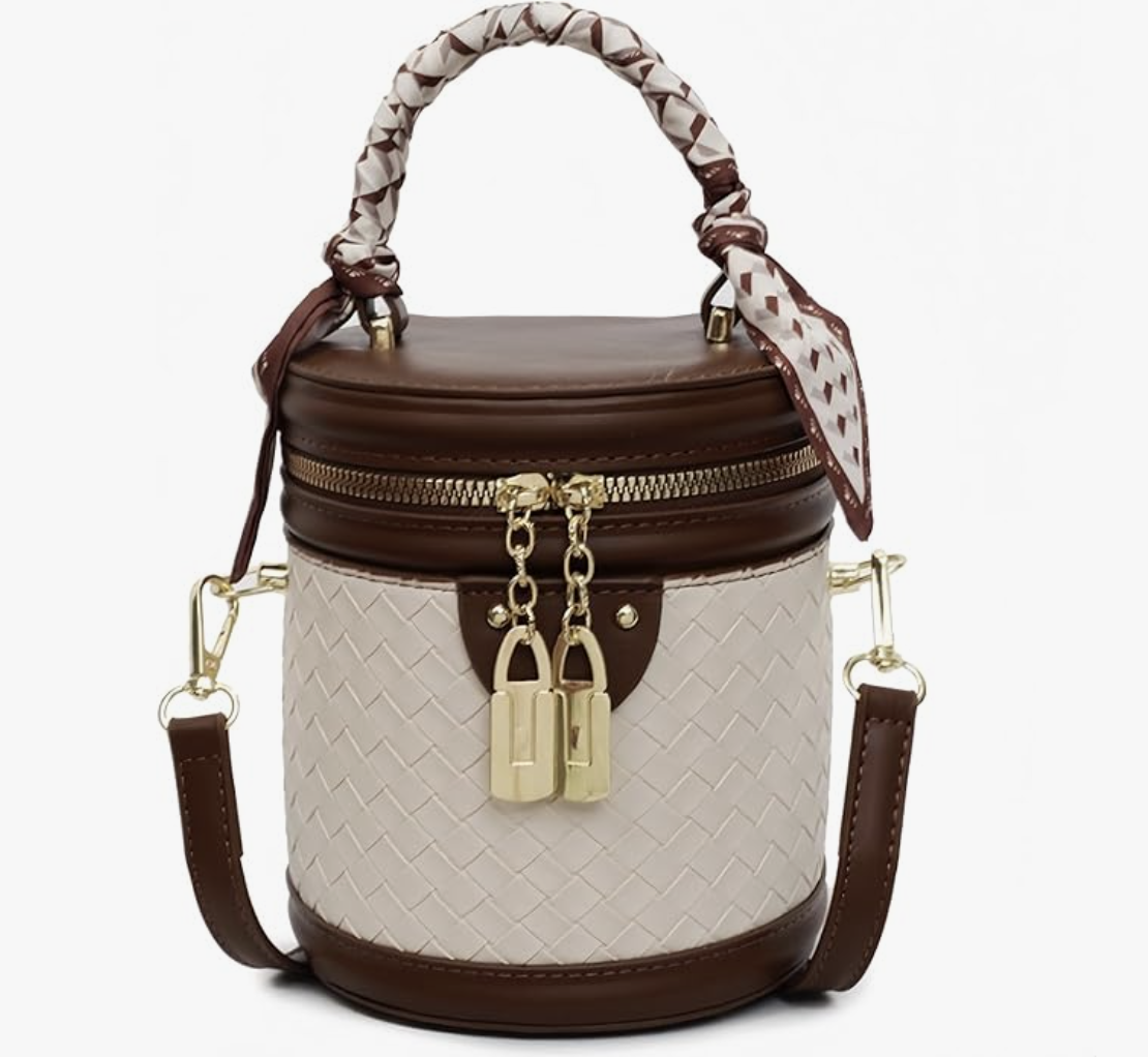 A structured mini bucket crossbody bag featuring a cream woven wicker body with dark espresso brown leather trim, gold padlock details, and a patterned scarf-wrapped top handle.