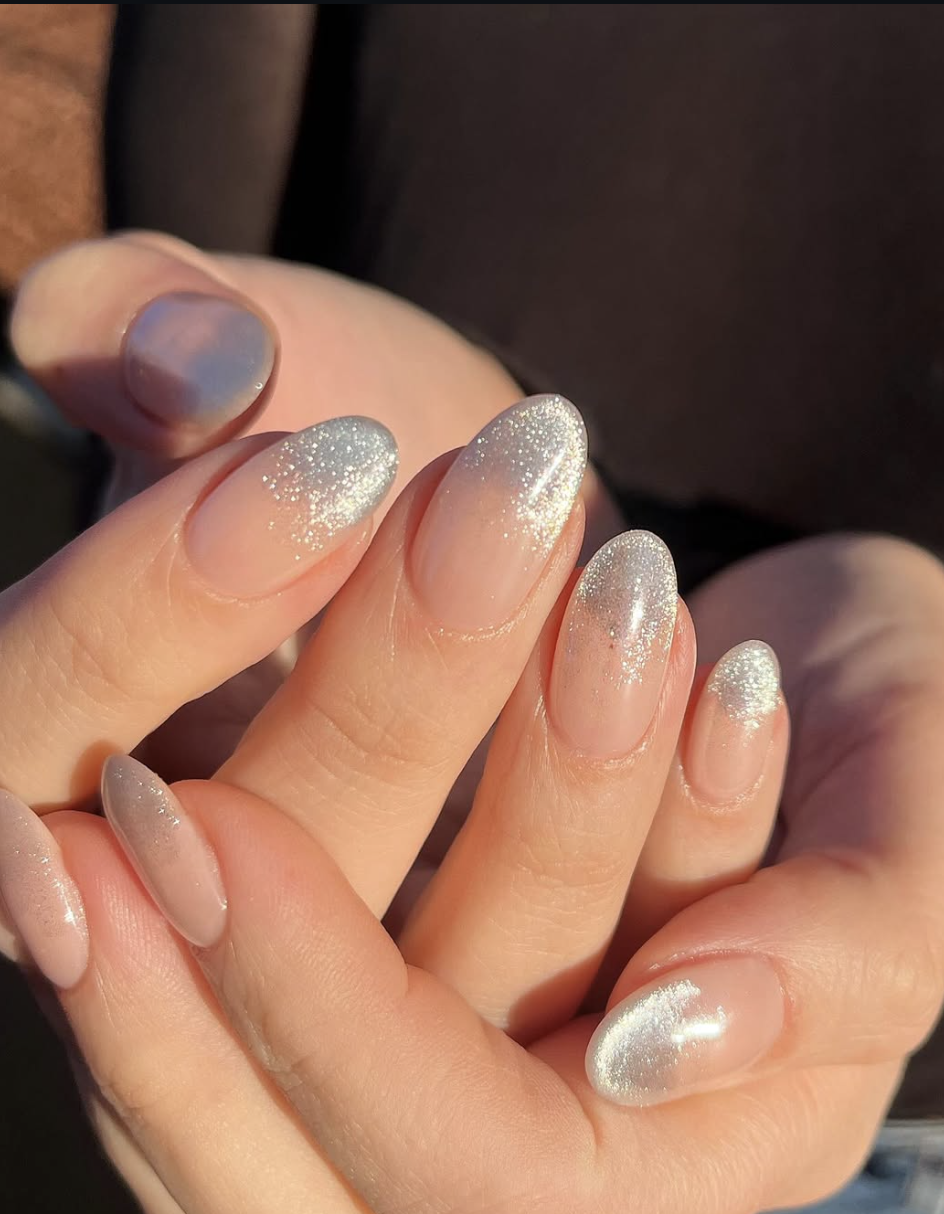 Long, oval-shaped nails featuring a translucent nude base with a dramatic silver glitter ombre fade concentrated at the tips, all finished with a luminous pearl chrome glaze.