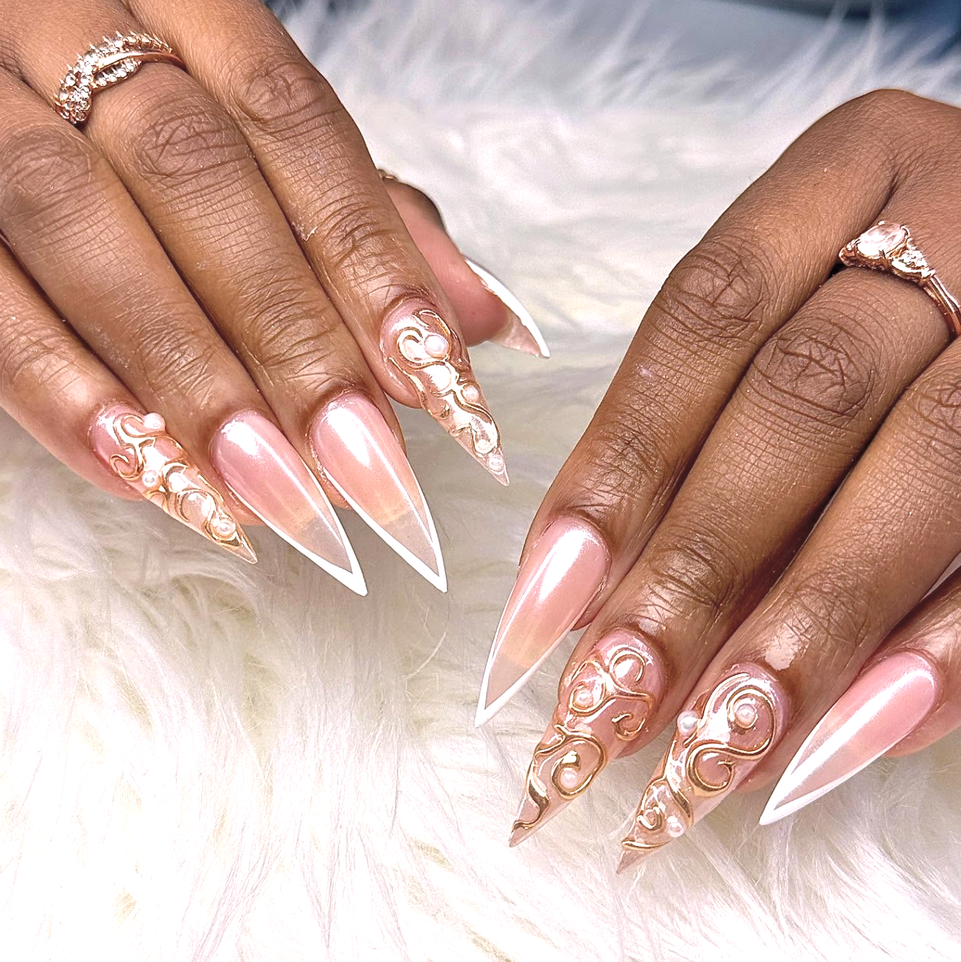 Extra-long stiletto nails with a pearlescent pink base, crisp white French tips, and 3D gold chrome swirls embellished with raised white pearls.