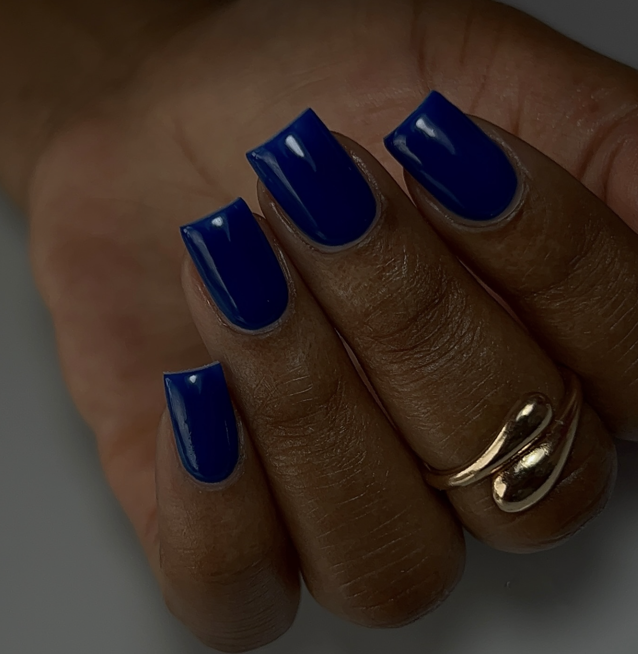 Close-up of short squoval nails featuring a glossy deep navy blue manicure paired with gold rings.