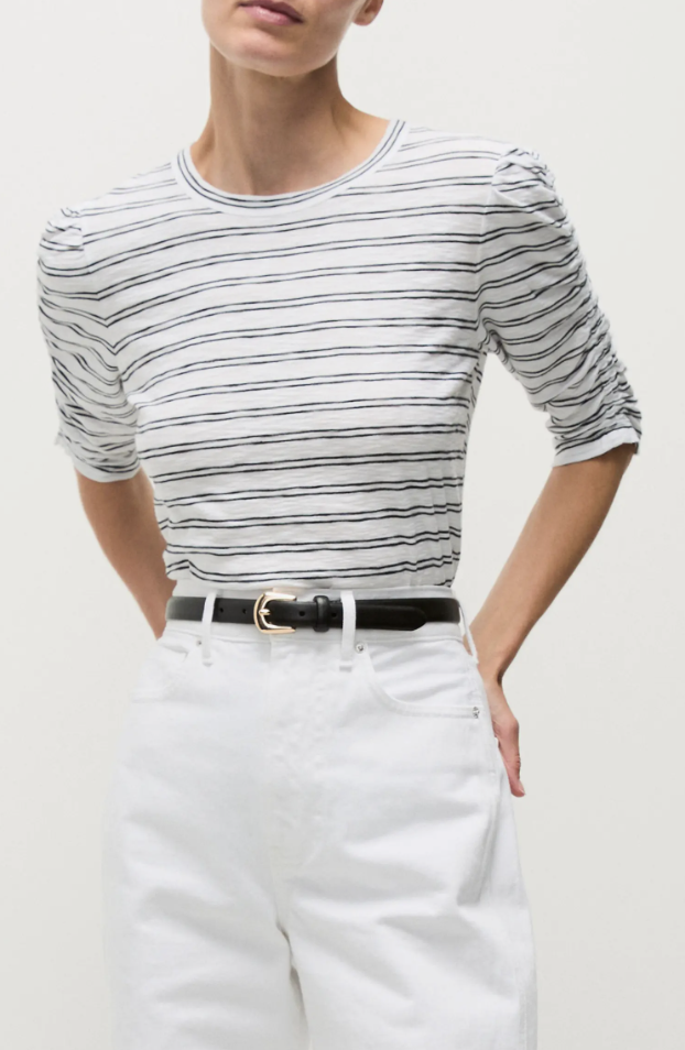Close-up of a woman wearing a black and white fine-striped puff-sleeve t-shirt tucked into high-waisted white jeans with a thin black leather belt.