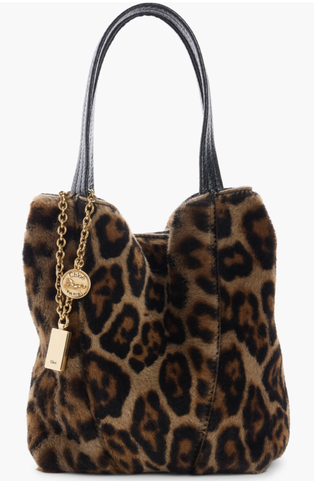 A leopard-print shearling tote bag featuring black leather handles and gold chain logo charms.