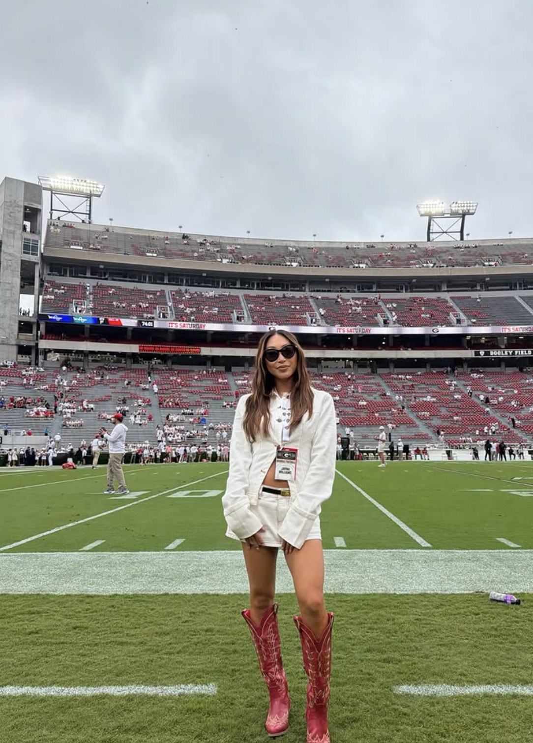 Woman at a Georgia football game wearing a white cropped jacket and shorts with red embroidered knee-high cowboy boots.