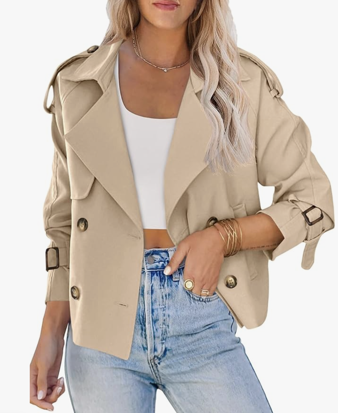 A woman wearing a tan cropped double-breasted trench coat with a high collar and buttoned cuffs, styled with a white bodysuit and light-wash denim jeans