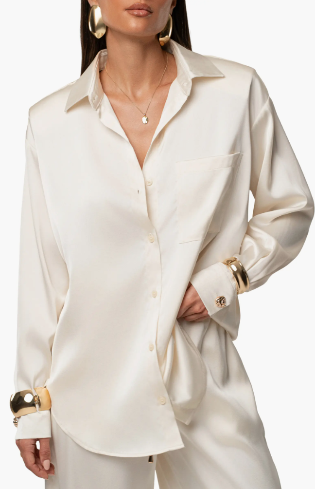 A woman wearing a cream satin button-down shirt tucked into brown trousers to demonstrate a polished color pairing.