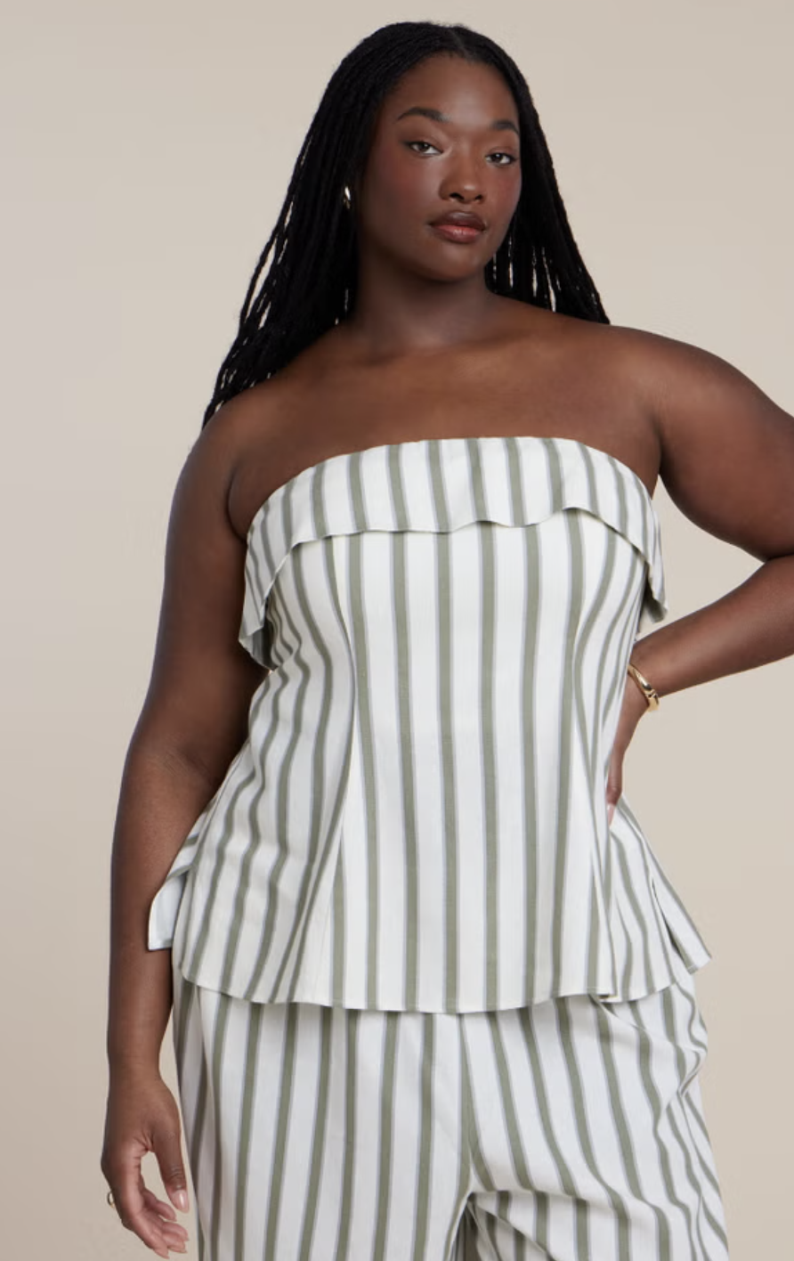 Plus-size woman wearing a strapless green and white striped peplum top with a ruffle detail.