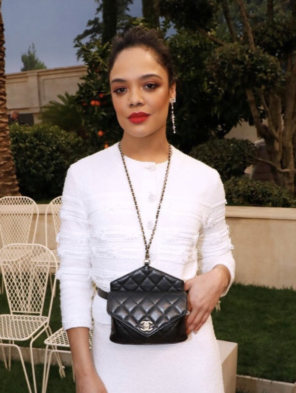 A close-up shot of Tessa Thompson in a white textured outfit, showcasing a Spring color season makeup look with a bright coral-red lip and clean, radiant skin.
