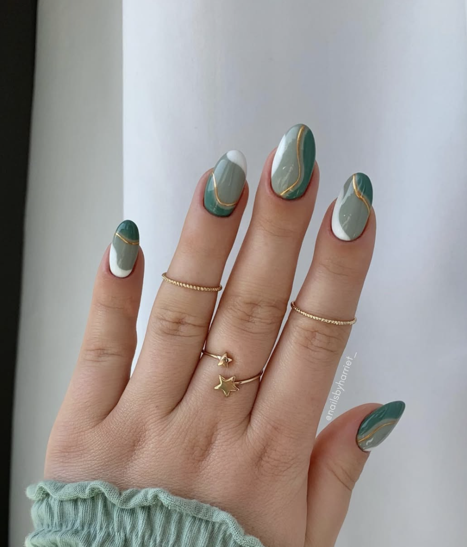 A close-up of almond-shaped nails featuring a mix of mint green and dark green polish with wavy gold metallic outlines.