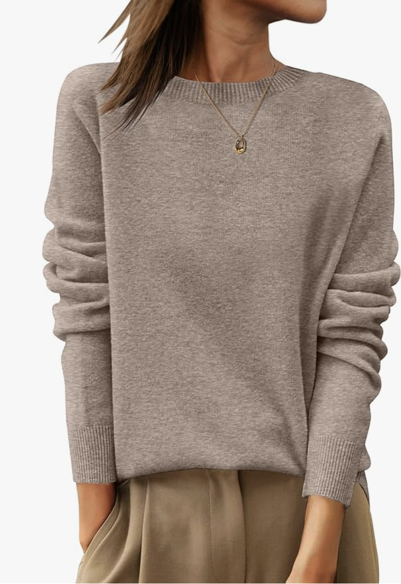 A woman wearing a taupe merino wool crewneck sweater with a gold pendant necklace, highlighting a high-quality, anti-pilling investment piece for a 2026 capsule wardrobe.