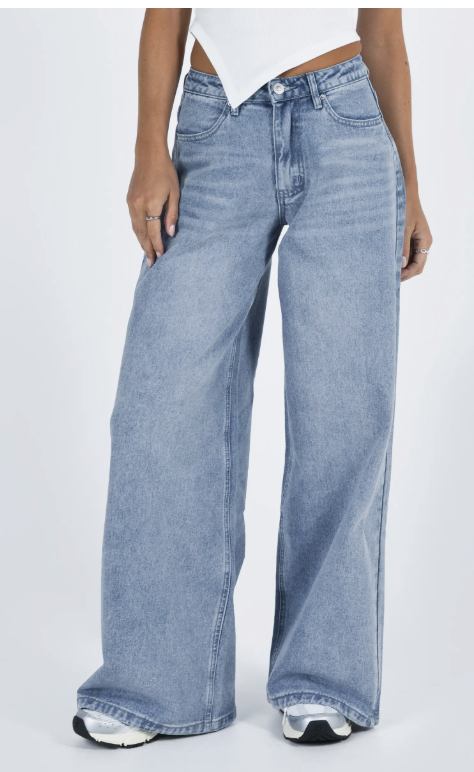 A close-up shot of a person wearing light-wash wide-leg baggy jeans that pool slightly over black and white athletic sneakers with a thick white sole.