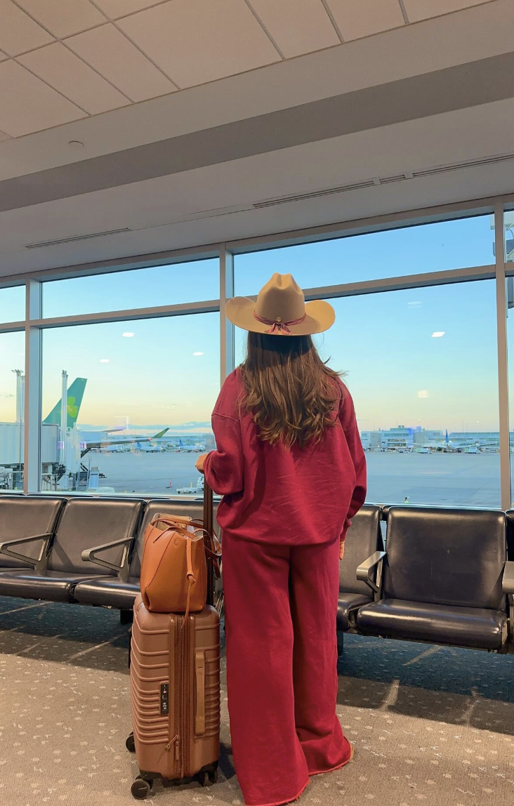 Red long-sleeve top and wide-leg trousers with a tan cowboy hat beside warm-toned luggage.