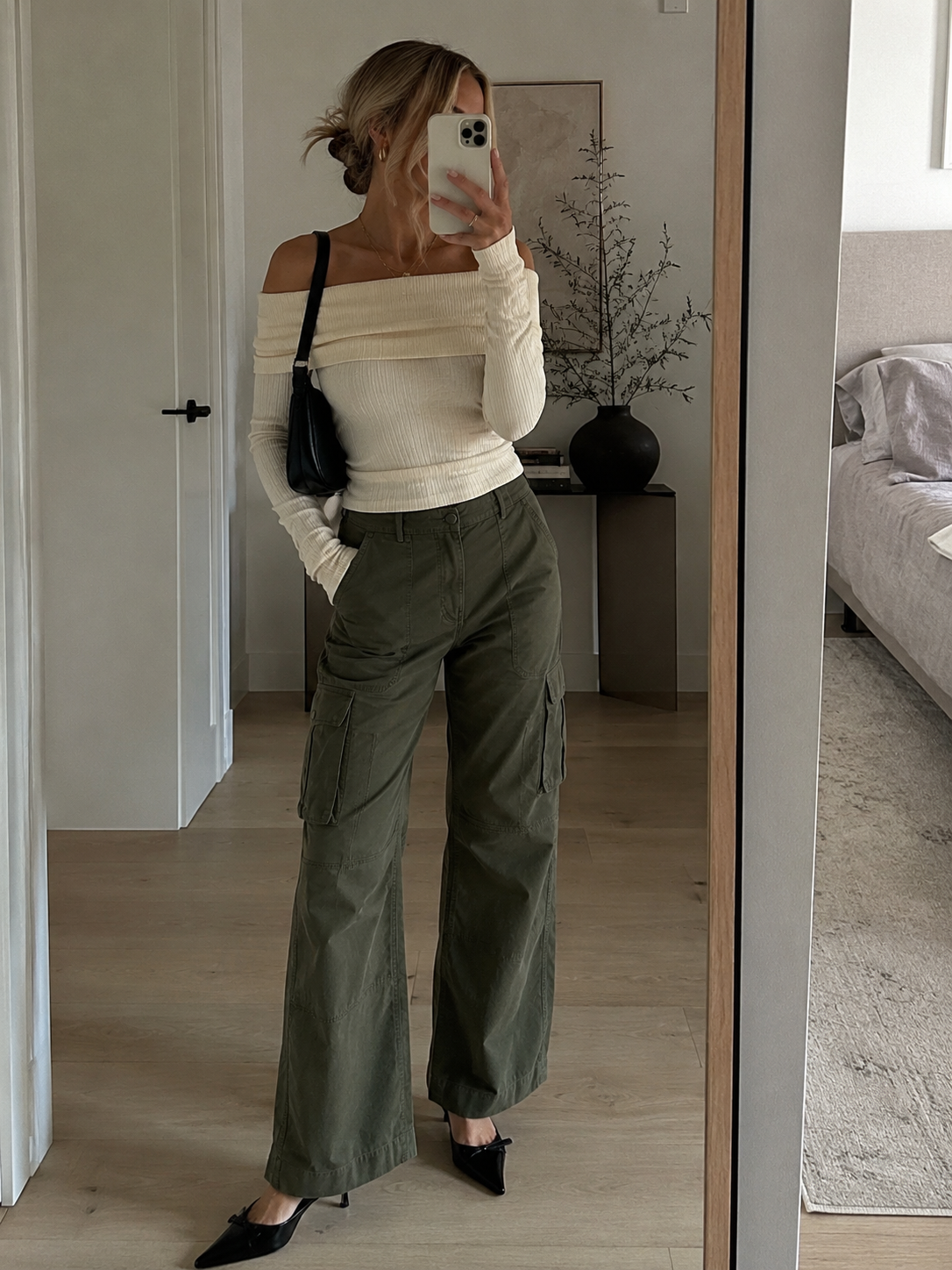 A person wearing a cream-colored off-shoulder long-sleeve ribbed top paired with olive green wide-leg cargo pants and black pointed-toe kitten heels.