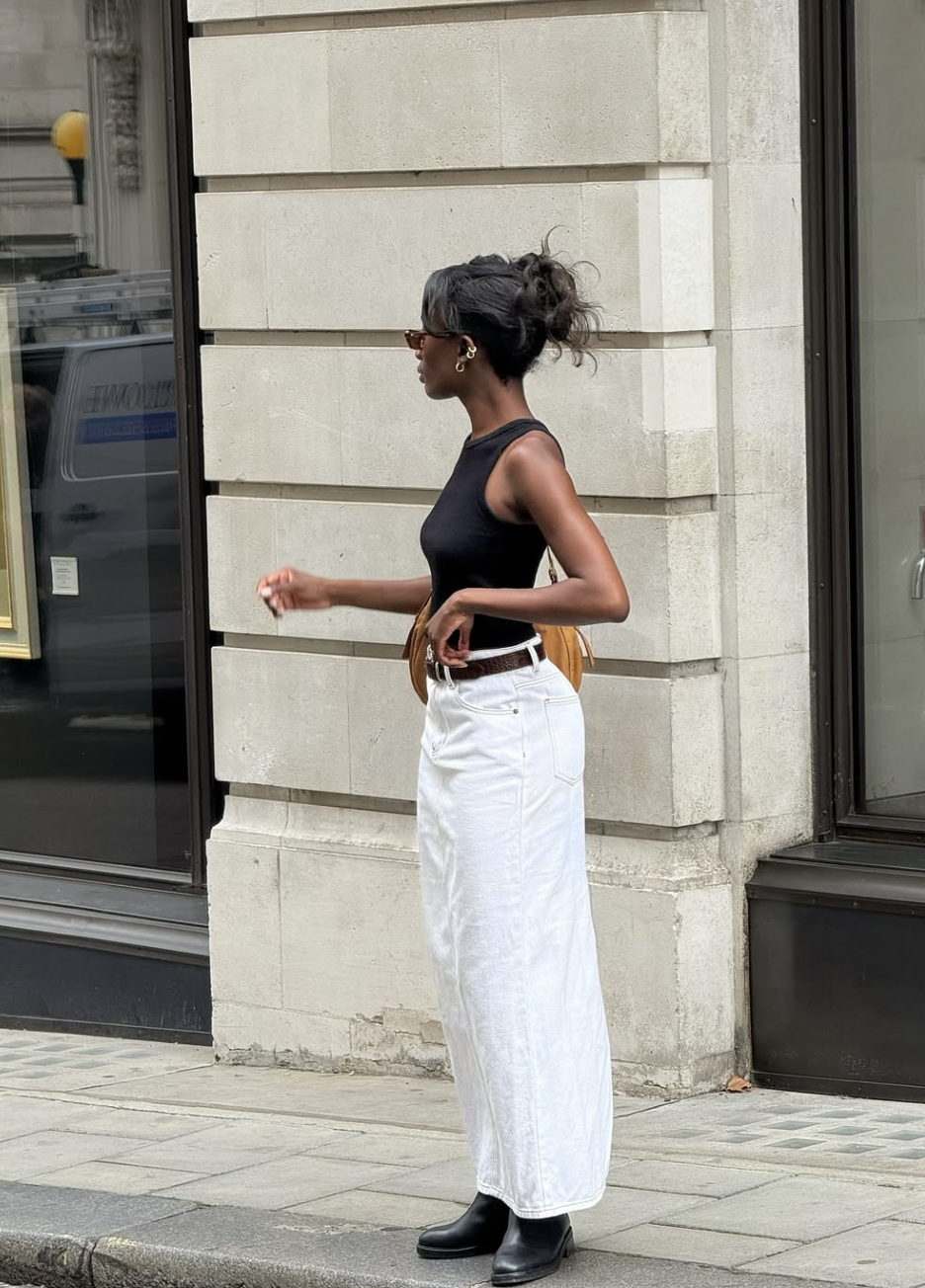 A woman wearing a black sleeveless ribbed bodysuit tucked into high-waisted white wide-leg jeans with a brown leather belt, styled for a modern everyday look.