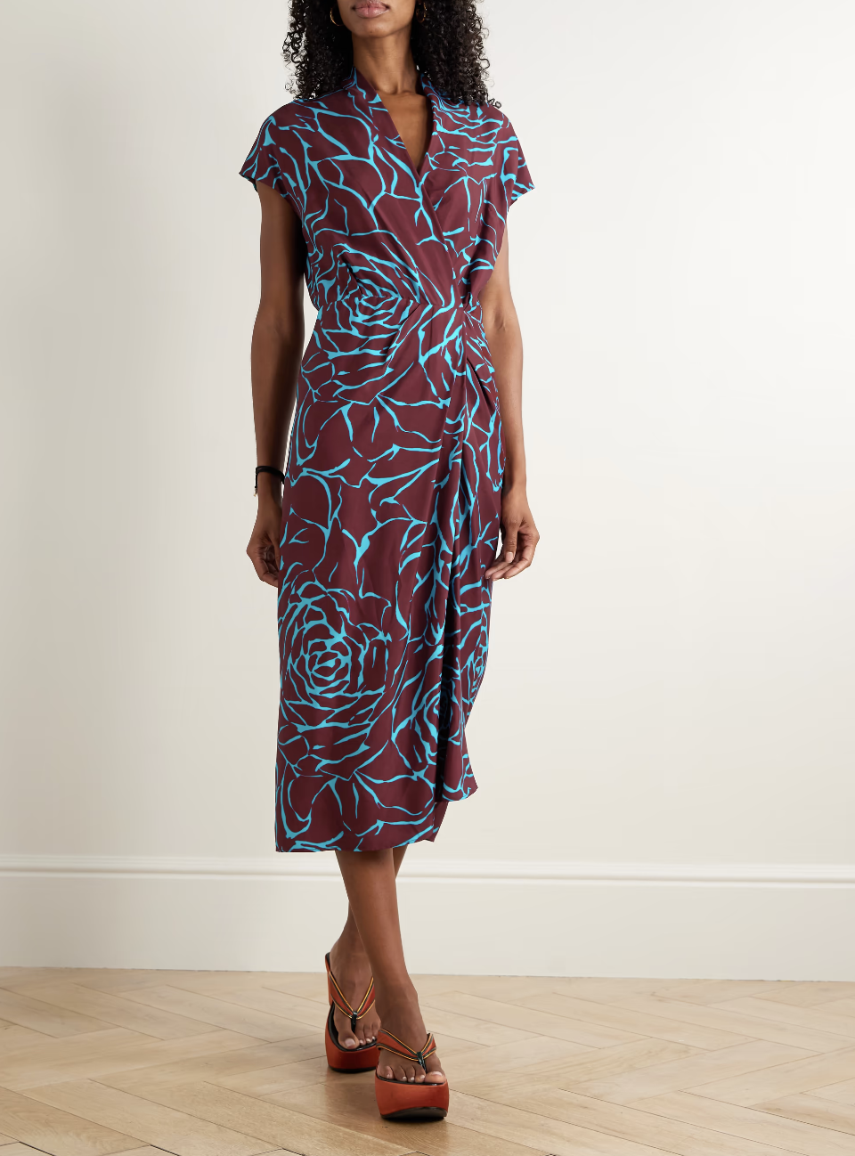 A woman wearing a Dries Van Noten wrap-effect floral-print satin midi dress in burgundy and teal, styled as an editorial wedding guest look.