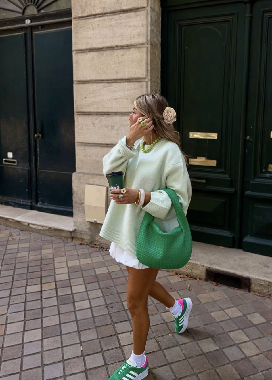 A woman wearing a light green oversized sweater and holding a bright green textured handbag and a coffee cup.