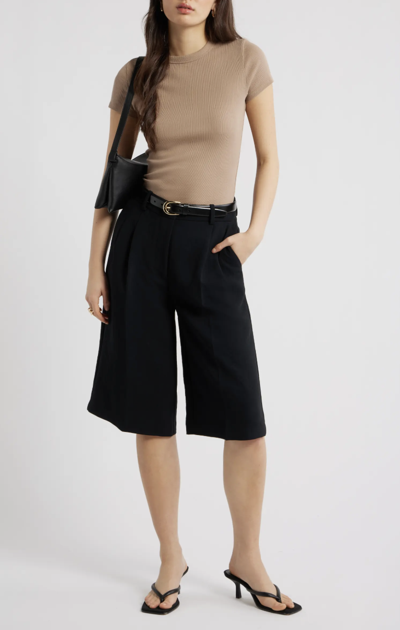 A woman wearing black wide-leg crepe culottes paired with a tan short-sleeve knit top and black heels.