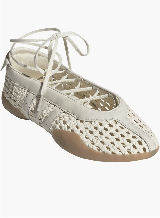 A close-up of a white woven leather ballet flat with thin lace-up ties and a gum rubber sole, showcasing the 2026 "Sneakerina" trend for a professional capsule wardrobe.