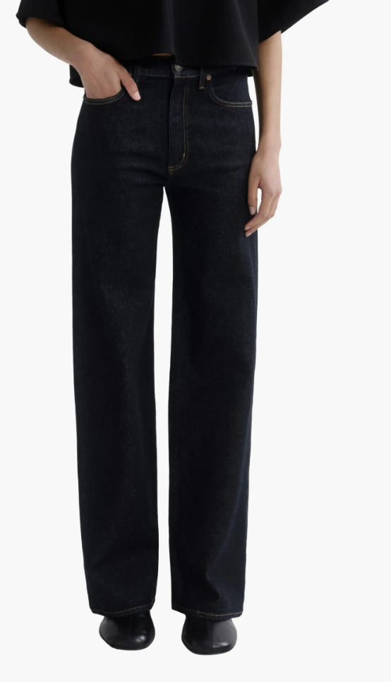 Woman wearing dark-wash straight-leg jeans with a black top and black leather loafers.