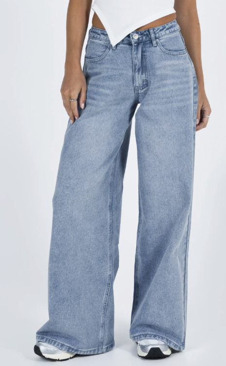 Close-up of a woman wearing light-wash, low-rise wide-leg baggy jeans paired with white sneakers to showcase a relaxed streetwear silhouette.