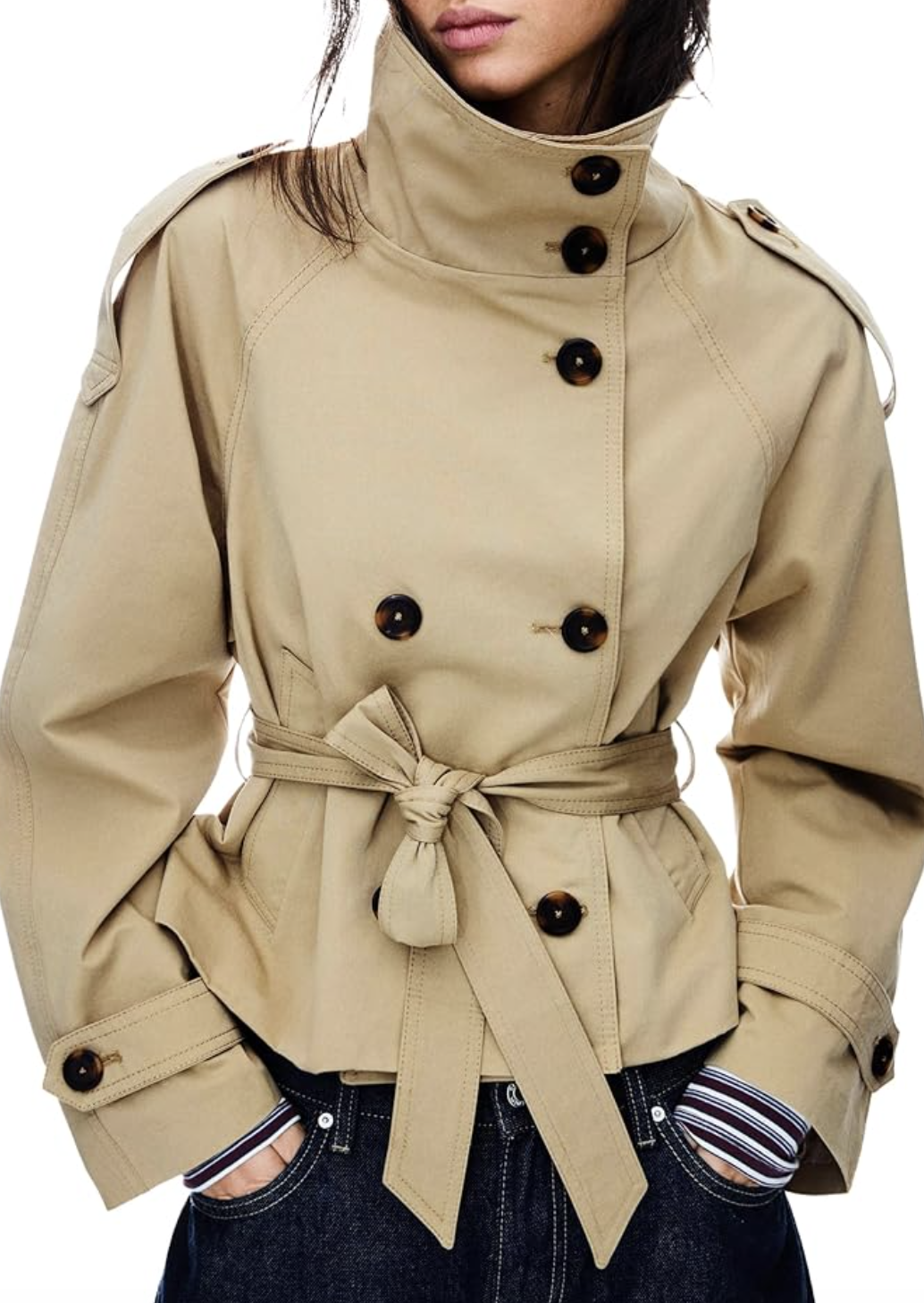 Close-up of a woman wearing a cropped khaki trench coat with dark brown buttons and a belted waist.