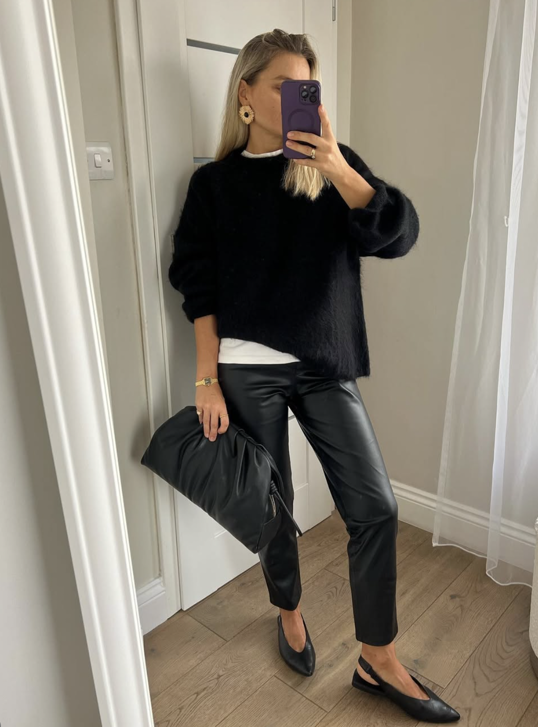 Woman wearing black slim leather pants with a fuzzy black sweater, white tee and a slouchy black clutch