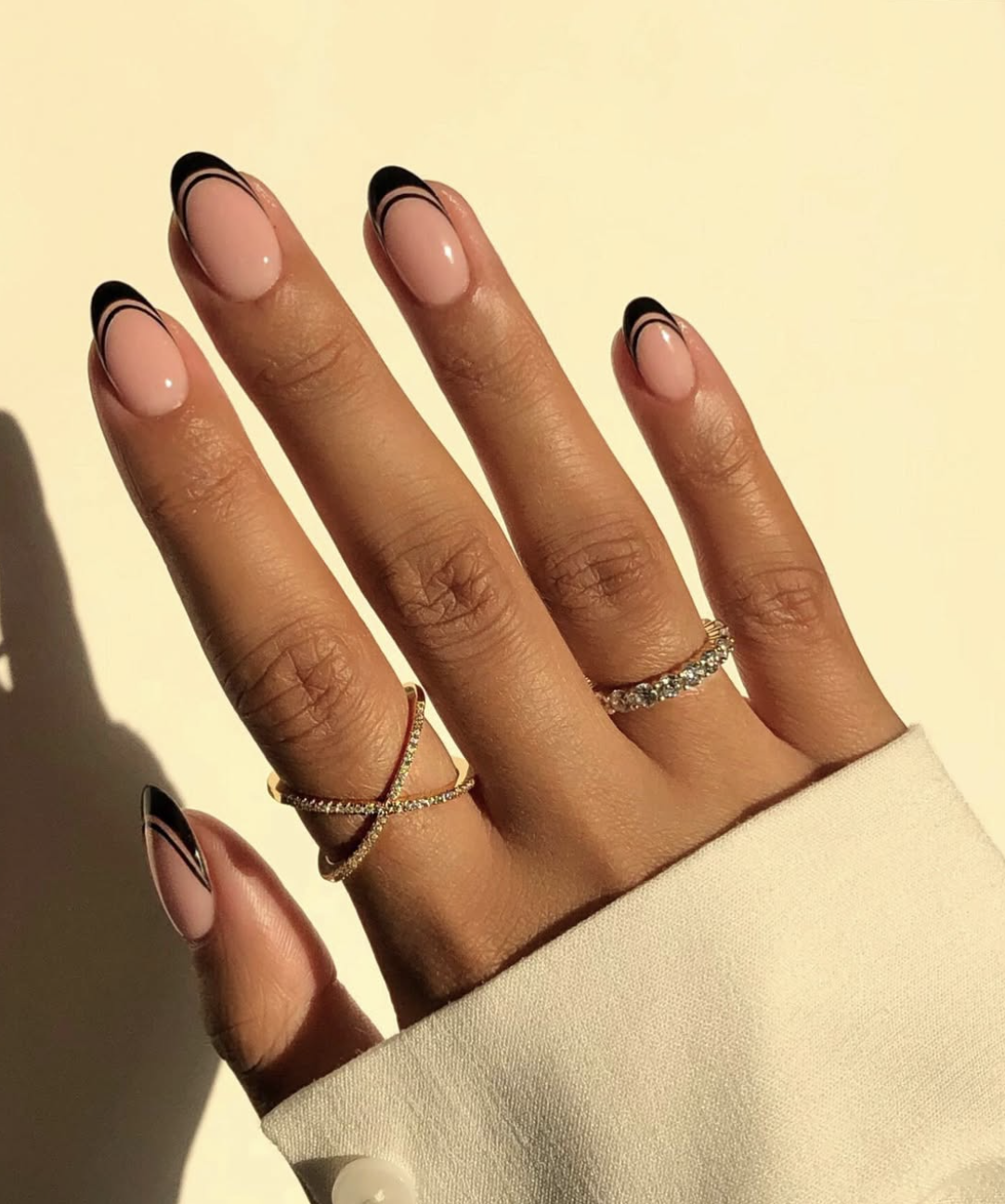 Close-up of short oval nails featuring a double-line micro French manicure with two ultra-thin black concentric curves over a sheer nude pink base.