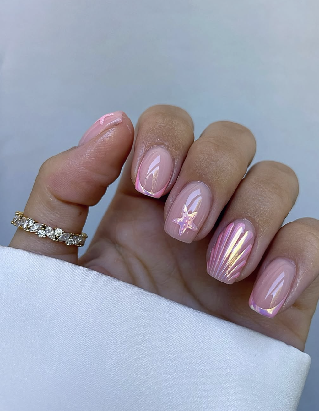 Short natural nails featuring a shimmering pink chrome base with subtle 3D ridged texture and luminous, iridescent star overlays that reflect a golden-green shift.