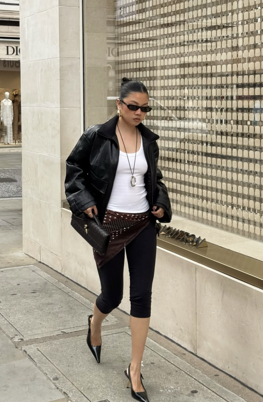 A 2026 street style look featuring a black leather jacket, black capri pants, and a heritage print silk scarf tied low on the hips as a belt.