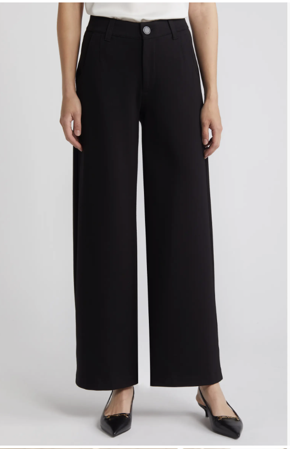 A close-up shot of a model wearing Wit & Wisdom Whitney Skyrise Flat-Front Wide-Leg Pants in black, styled with a tucked-in white top to highlight the clean, flat-front waistband.