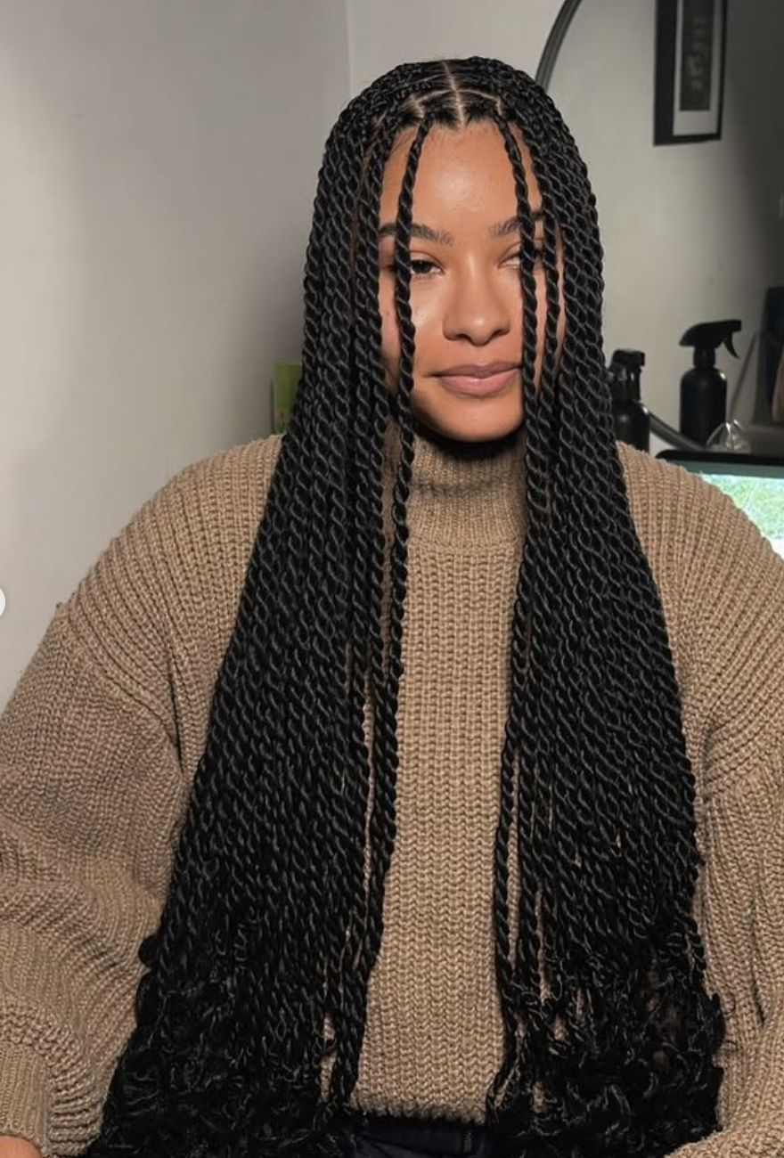A woman with an oval face shape wearing long, waist-length Senegalese twists with a middle part.