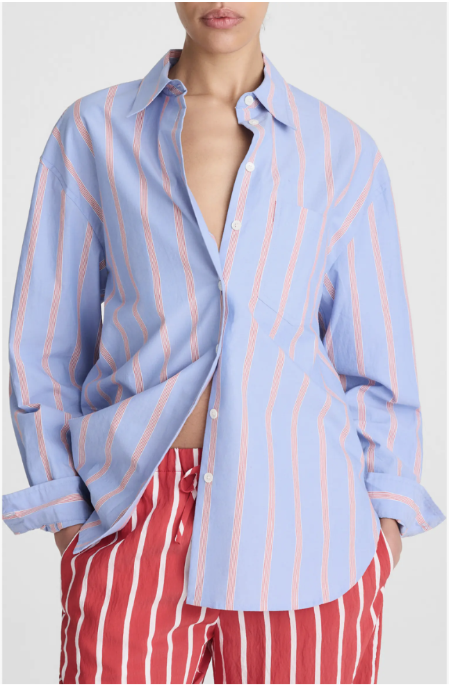A woman wearing an oversized light blue and white vertical striped button-down shirt layered over bright red and white striped trousers.
