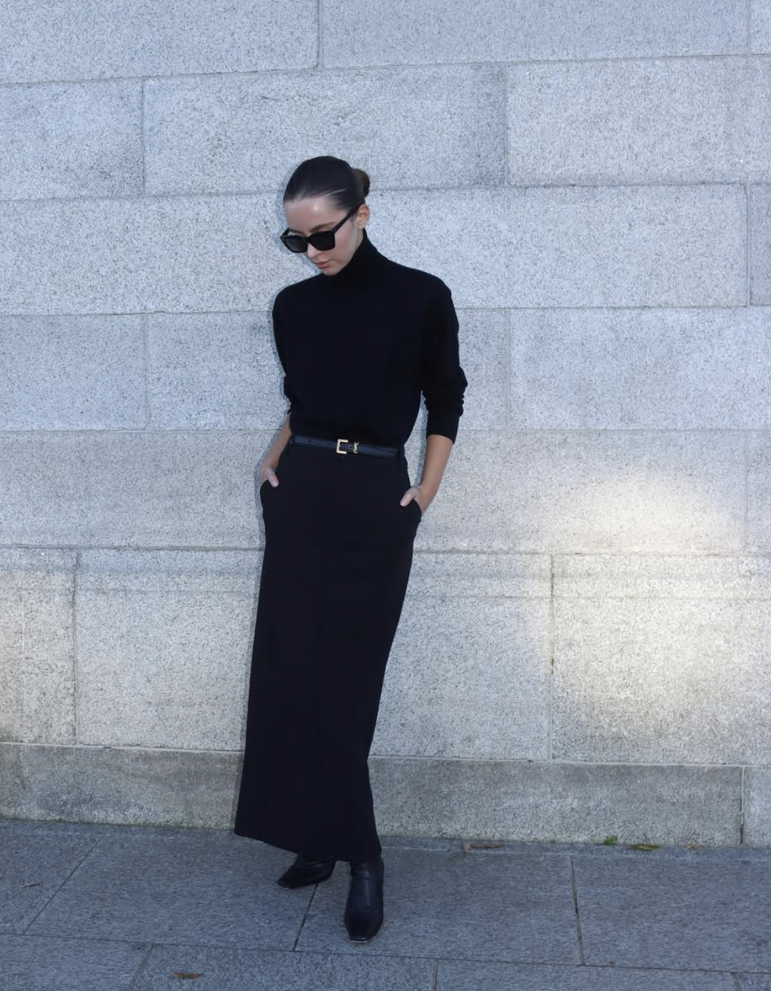 Woman wearing a black knit midi skirt, black turtleneck, slim belt and black ankle boots
