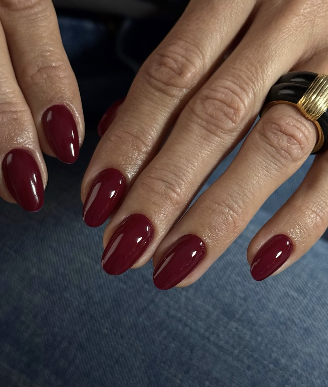 A close-up of short, oval-shaped nails with a high-shine, deep cherry red polish.
