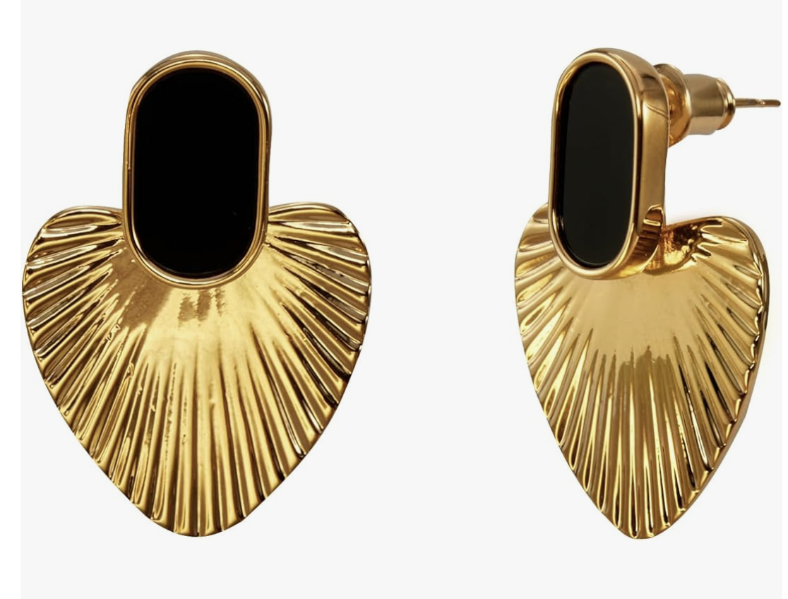 A pair of large, ribbed gold heart-shaped statement earrings with a black oval stud base, styled as a bold accessory for a luxury resort evening look.