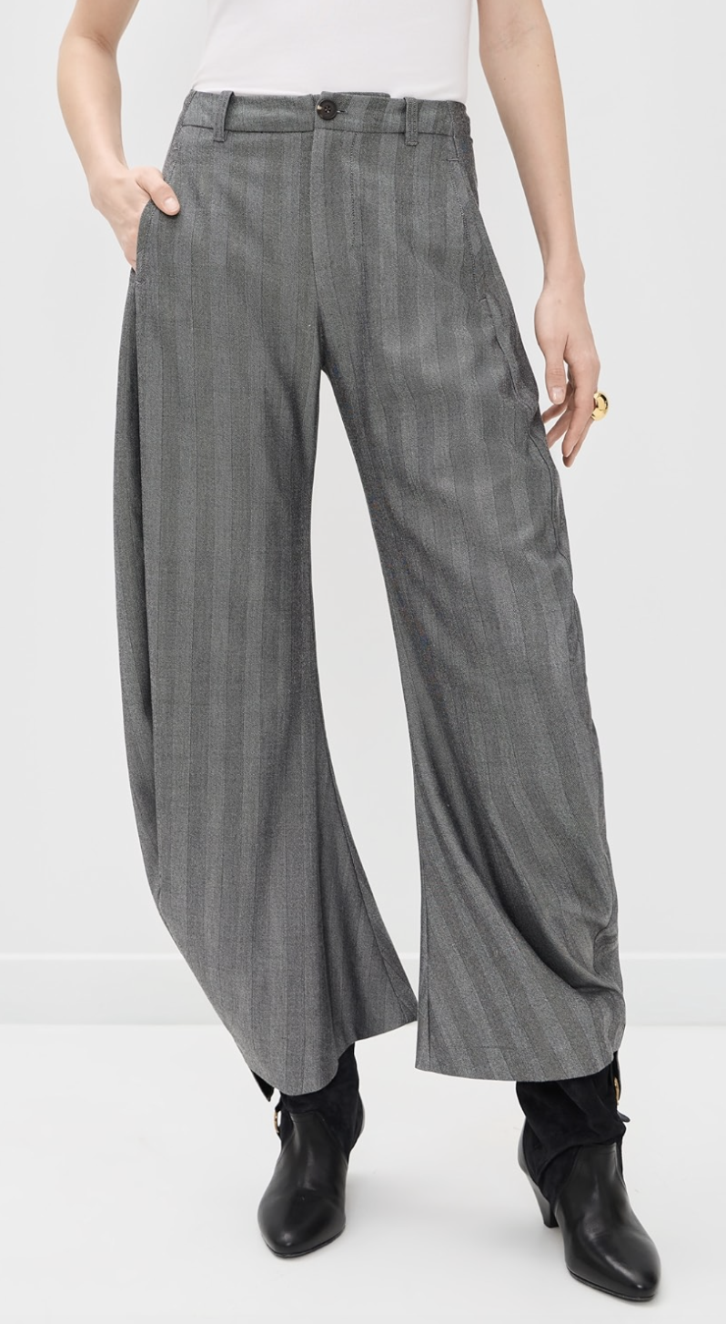A person wearing high-waisted, wide-leg grey pinstripe trousers paired with black pointed-toe ankle boots.