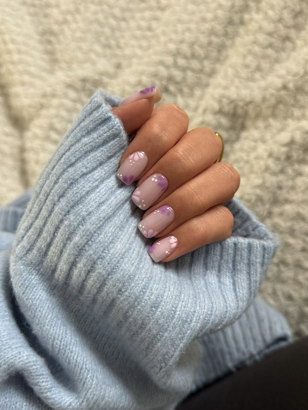 Short square nude nails with minimalist hand-painted purple and white flower petals scattered across the nail.